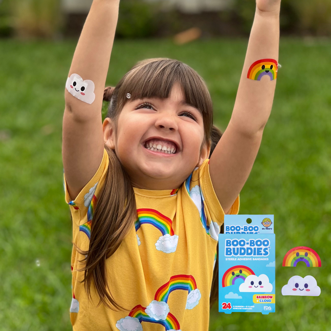Happy child raising her arms while wearing Boo Boo Buddies fun and colorful kids bandages outdoors.