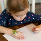Child drawing at a table while wearing a Boo Boo Buddies fun and colorful kids bandage on her hand.
