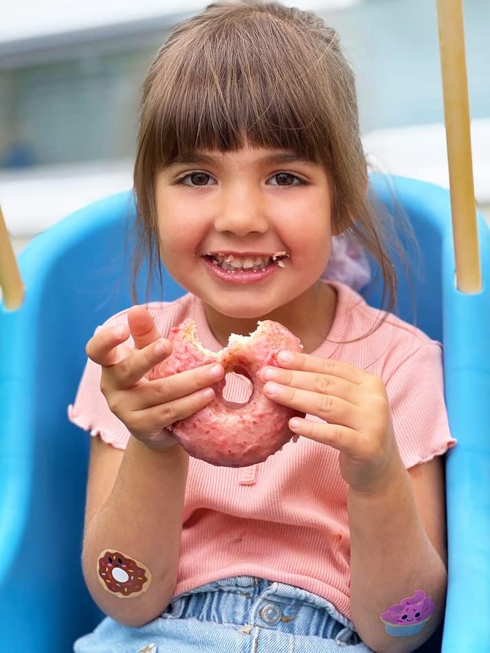 Smiling child eating a snack while wearing Boo Boo Buddies fun and colorful kids bandages on her arms.
