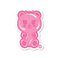 A pink die-cut vinyl sticker in the shape of a gummy bear character with a bow and arms, designed for use as a decal.