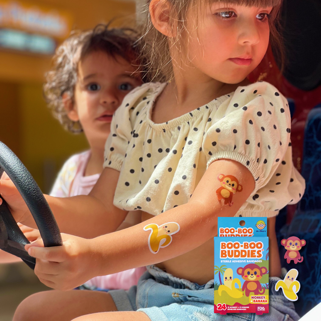 Child wearing Boo Boo Buddies monkey and banana bandages on arm, waterproof bandaids for playful kids who love fun healing comfort.
