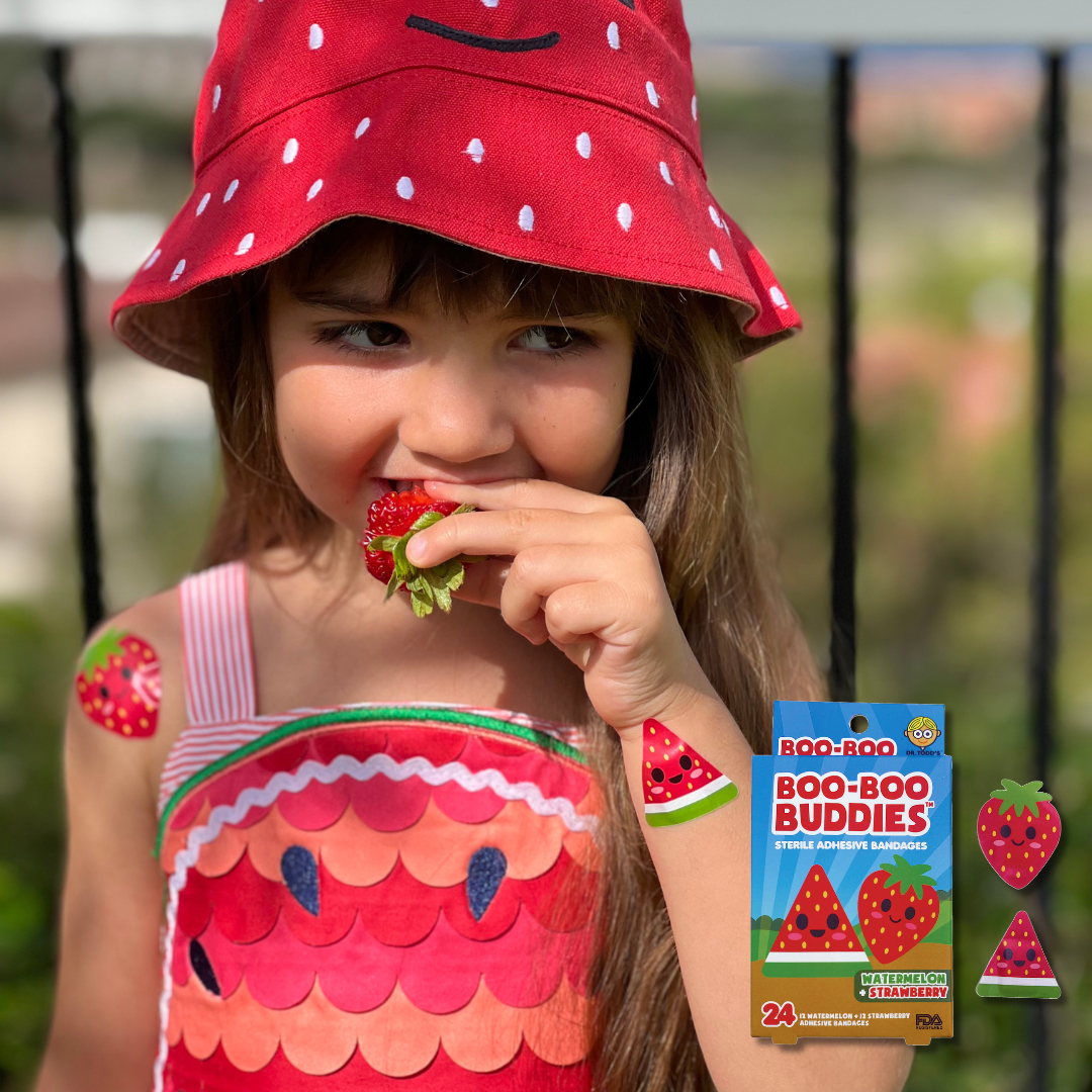 Child smiling outdoors while wearing Boo Boo Buddies fun and colorful kids bandages on her arms.”
