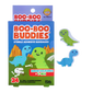 A colorful box of Boo-Boo Buddies bandages featuring two cute dinosaur shapes: a smiling green T-Rex and a blue Brontosaurus. The packaging shows a fun prehistoric scene with orange mountains and a dinosaur skeleton. The box contains 24 bandages (12 of each design) and emphasizes that they are sterile
